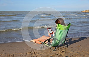 Girl reads a book on a modern ebook on the deckchair while relax