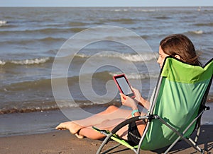 Girl reads an ebook on the deckchair relaxing by the sea with ba