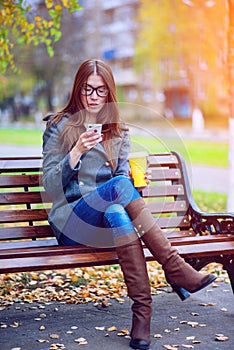 Girl reads sms, rewritten smartphone outdoors in spring or autumn, on the bench, with coffee tea, breakfast, concep