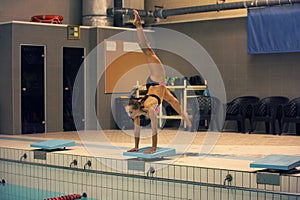 Girl ready to jump into indoor sport swimming pool. standing on arms with legs up