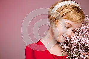 A girl in red against a pink wall with a bouquet of flowers near her face.