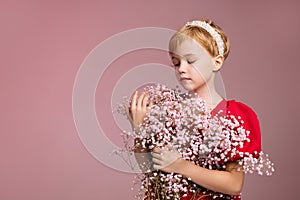 A girl in red against a pink wall with a bouquet of flowers near her face.