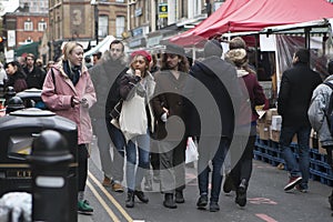 Girl in red beret and man with long hair in black hat dressed in cool Londoner style walking in Brick lane, a street popular among