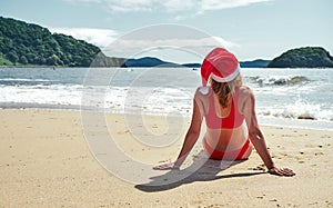 A girl in a red bikini and a santa hat is sunbathing on a sandy shore. Christmas in countries with a warm climate.