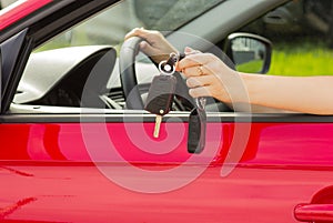 A girl in a red car demonstrates the keys to a new car, the concept of buying a vehicle