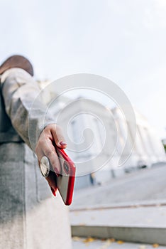 Girl with a red cell phone in hand in a cityscape. Phone close up