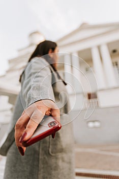 Girl with a red cell phone in hand in a cityscape. Phone close up