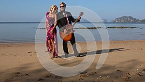 Girl in red clasps to guitarists breast on beach at dawn