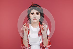 Girl in red clothes crossed her fingers in a hope isolated in a studio.