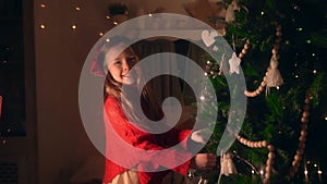 Girl in red clothes decorating big green Christmas tree