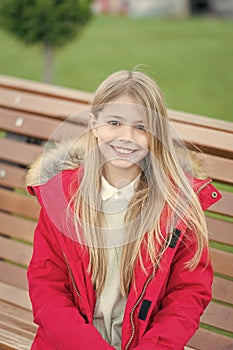 Girl in red coat sit on bench in park