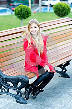 Girl in red coat sit on bench in park