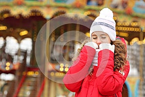 A girl in a red down-padded jacket and white hat closing his eyes dreams of a miracle.  Boke and flush in the background. Copy