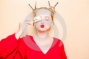 Girl in a red dress on a beige background. A woman eats with chopsticks for sushi, closes her eyes with them and grimaces, smiles