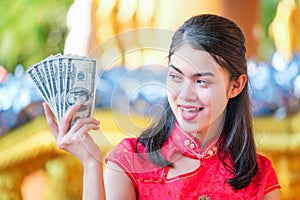 The girl in the red dress of Chinese descent is happy with red envelope with the dollar