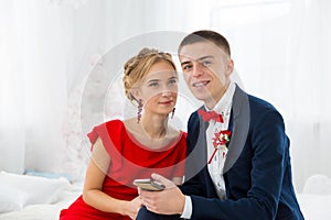 A girl in a red dress with a guy holding a mobile phone.