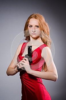 Girl in red dress with handgun against gray