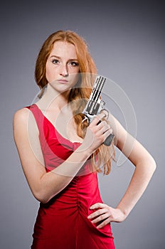 Girl in red dress with handgun against gray