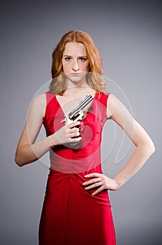Girl in red dress with handgun against gray