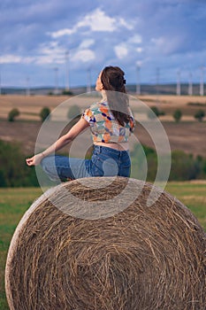 Girl in a red dress near a round bale of straw