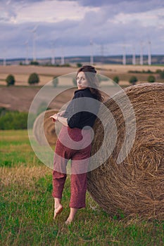 Girl in a red dress near a round bale of straw