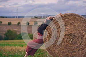 Girl in a red dress near a round bale of straw