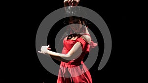 Girl in red dress performs elegant movements with her hands in dance. Black background