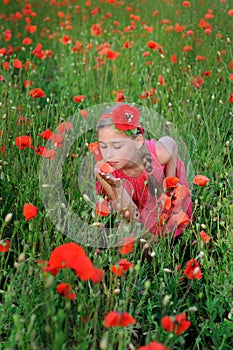 Girl in a red dress on the poppy field smelling a flowers