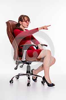 A girl in red dress and red glasses sits in an office chair and gestures, pointing finger somewhere