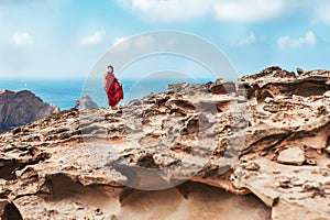Girl in red dress among rocks and cliffs along the Coast of Algarve