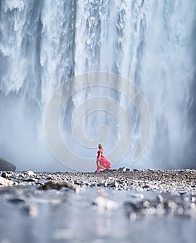 Girl in red dress on the Skogafoss waterfall background. Travelling on Iceland. Tourist in the famouns place in Iceland.