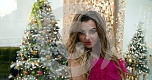 A girl in a red dress is walking near the Christmas tree at home. Beautiful girl next to the Christmas tree. Blonde