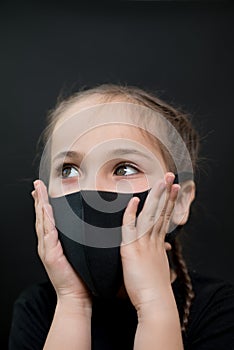 Girl with red eyes and black a medical mask on a black background, copy space. Concept of people who are isolated in a coronavirus