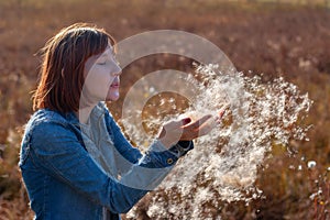 A girl with red hair blows on the scattering fluff in her hands