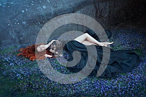 Girl with red hair lying on grass in dark forest, black queen lost in battle, charming lady in long black royal dress