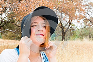 Girl With Red Hair, Overalls and Black Hat Standing in Field