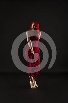 A girl with red hair, in a red dress posing on a dark background