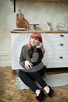 A girl with red hair sits on  rug in the kitchen, self-isolation, rest in quarantine, being at home, not going out