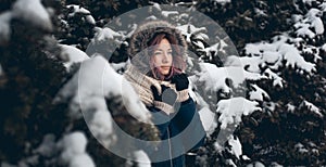 Girl with red hair stands in a blue jacket with a hood among the snow covered fir trees