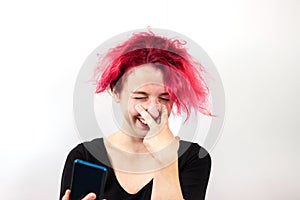 A girl with red hair talks on a video link on a smartphone and makes a face pulling down her eyelids with her hands
