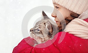 A large labrador dog and a cat in winter on a walk with a young woman in a snowy field