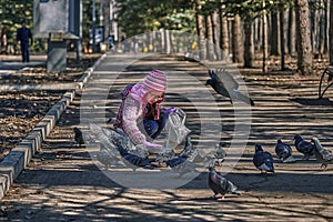 Girl in a red jacket, hat and glasses chasing pigeons in the park.