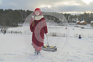 A girl in a red jacket walks down a snow-covered slide with tubing