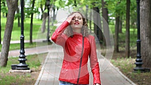 Girl in red leather jacket smiling in a park and looking at camera telling something