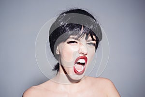 Girl with red lips makeup wearing black wig isolated on gray background. Woman with angry face yelling at somebody