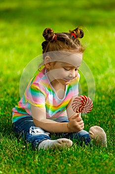 Girl with red lollipop sits on the summer grass