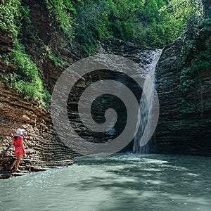 Girl in red looks at the waterfall Maiden spit on the stream Rufabgo, Adygea, Russia