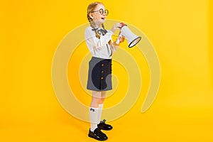 Girl with red pigtails on a yellow background. A charming girl in round transparent glasses is holding a loudspeaker in