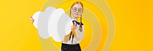 Girl with red pigtails on a yellow background. A charming girl in round transparent glasses is holding a white cloud in