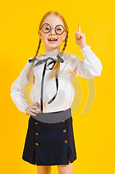 Girl with red pigtails on a yellow background. A charming girl in round transparent glasses raised her index finger up.